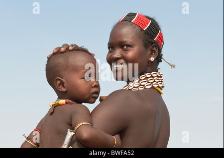 Jeune femme Hamar portant des colliers faits de cauris et perles en plastique et tenant son bébé dans les bras, l'Ethiopie Banque D'Images