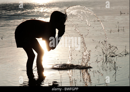 Jeune Indien l'eau potable et le lavage dans un lac en Inde au coucher du soleil. Silhouette. L'Andhra Pradesh, Inde Banque D'Images