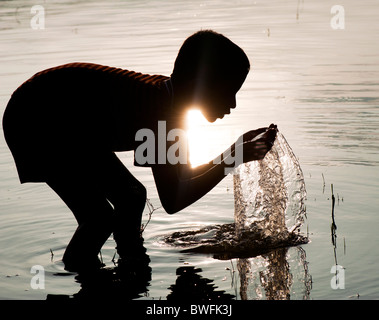 Jeune Indien l'eau potable et le lavage dans un lac en Inde au coucher du soleil. Silhouette. L'Andhra Pradesh, Inde Banque D'Images