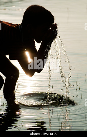 Jeune Indien l'eau potable et le lavage dans un lac en Inde au coucher du soleil. Silhouette. L'Andhra Pradesh, Inde Banque D'Images