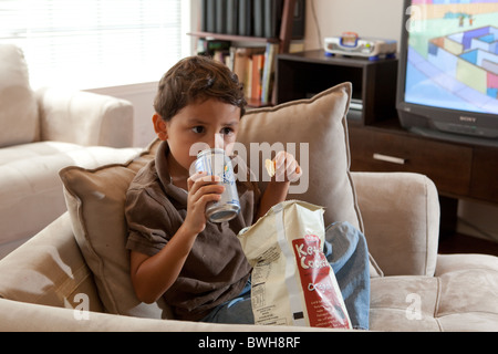 Quatre-année-vieux garçon mexico-mange de croustilles et de boissons gazeuses sips dans le salon à son domicile à Austin, Texas Banque D'Images