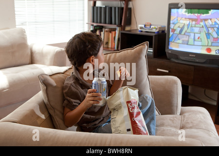 Quatre-année-vieux garçon mexico-mange des croustilles, gorgées de boisson gazeuse et regarde la télévision dans le salon à son domicile à Austin Banque D'Images