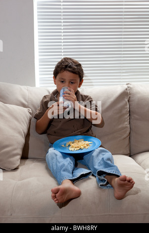 Quatre-année-vieux garçon mexico-mange les chips de pomme de terre pour une collation sur le canapé dans le salon à son domicile à Austin, Texas Banque D'Images
