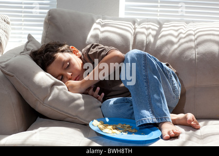 Quatre-année-vieux garçon mexico-mange les chips de pomme de terre pour une collation sur le canapé dans le salon à son domicile à Austin, Texas Banque D'Images