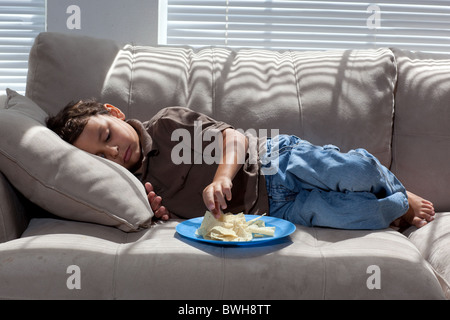 Quatre-année-vieux garçon mexico-mange les chips de pomme de terre pour une collation sur le canapé dans le salon à son domicile à Austin, Texas Banque D'Images