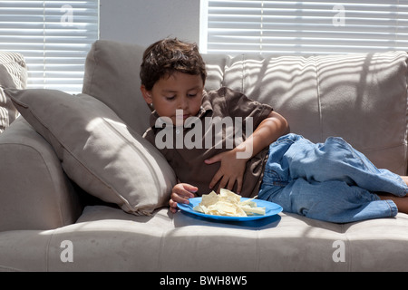 Quatre-année-vieux garçon mexico-mange les chips de pomme de terre pour une collation sur le canapé dans le salon à son domicile à Austin, Texas Banque D'Images