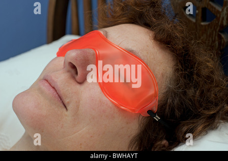 Femme portant un masque gel pour les yeux de refroidissement qui refroidit autour des yeux après une fin de nuit Banque D'Images