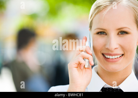 Portrait de jolie femme qui parle d'affaires par téléphone mobile et à la recherche à l'appareil photo avec sourire Banque D'Images