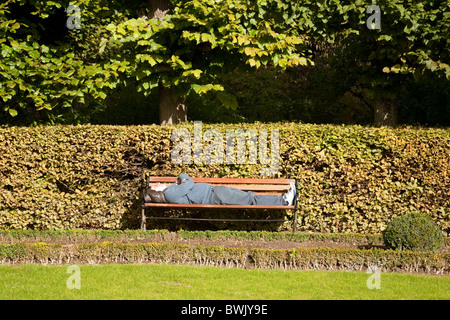 Un homme endormi sur un banc de parc dans l'après-midi soleil Banque D'Images