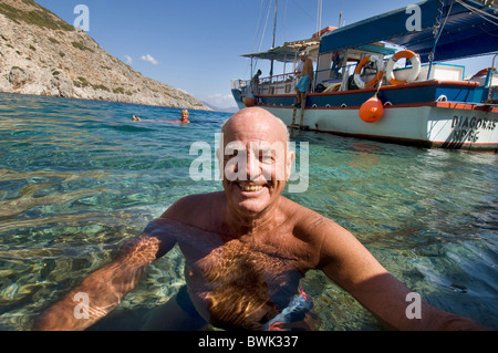 En forme, en bonne santé, tannées older man smiling at camera comme il nage dans la mer au large de l'île grecque de Symi Banque D'Images