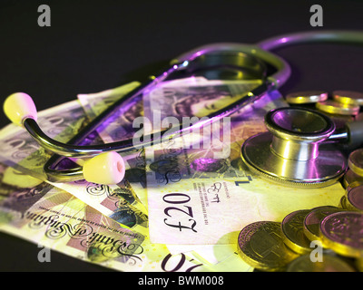 British pound coins empilés en arrière-plan sur un lit de notes de 20 livres avec un stéthoscope Banque D'Images