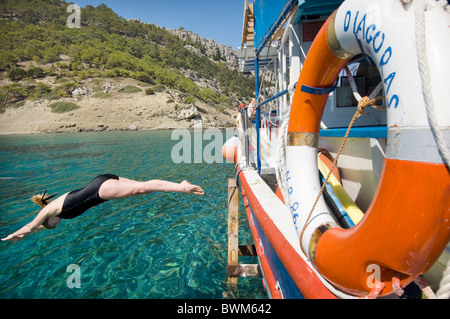 Une femme plonge vers le côté d'un bateau de plaisance grec 'Diagoras' dans l'île de Symi dans la mer Egée, en Grèce. Banque D'Images