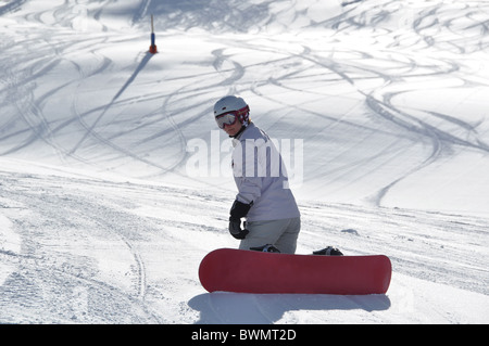 Les femmes d'âge moyen snowboarder portant casque et lunettes de neige poudreuse, à genoux sur la colline escarpée - tourné à Livigno, italien Banque D'Images