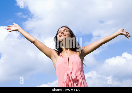 Portrait of happy girl louant Dieu avec ses yeux fermés et les bras levés sur fond de ciel nuageux Banque D'Images