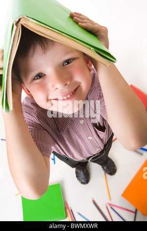 Photo de Fisheye garçon diligent avec livre sur sa tête alors qu'à faire leurs devoirs Banque D'Images