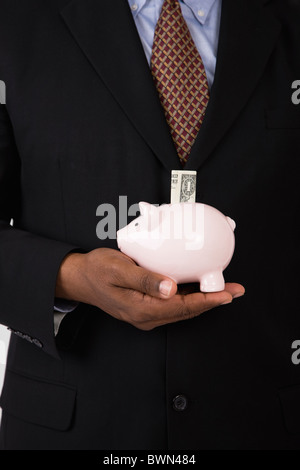 États-unis, Illinois, Metamora, Man holding piggy bank avec billet de un dollar, mid section Banque D'Images