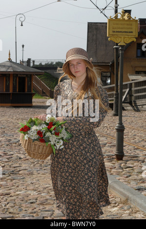 Fille en robe gay et chapeau avec panier de fleurs dans ses mains dans un style ancien. Banque D'Images