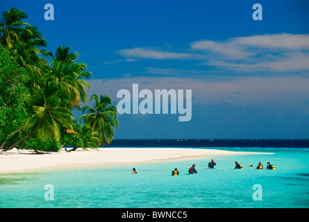 Groupe de plongeurs de l'école de plongée assis dans les eaux aqua avec les réservoirs d'air au large plage de sable fin sur l'île de Soneva Gili aux Maldives Banque D'Images