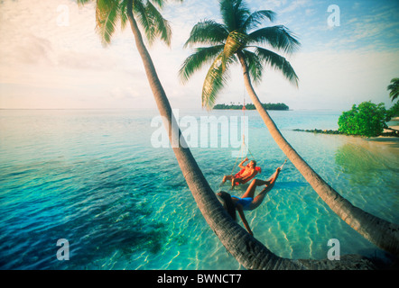 Couple hanging sous des palmiers au coucher du soleil sur Meeru Island aux Maldives Banque D'Images