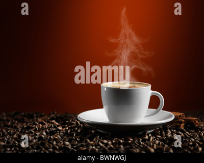 L'augmentation de vapeur en forme d'arbre de Noël autour d'une tasse de café latte comité permanent sur les grains de café isolé sur fond rouge foncé Banque D'Images