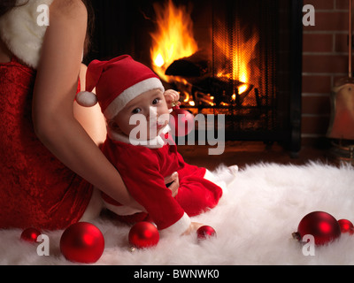 Mère et un petit bébé garçon assis en face d'une cheminée dans des costumes de Noël. Banque D'Images