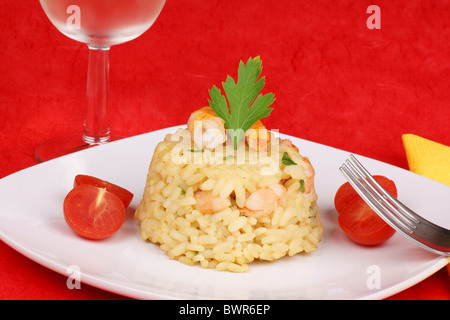 Risotto aux crevettes servi sur une plaque blanche et décoré avec des tomates cerises. Studio shot sur fond rouge Banque D'Images