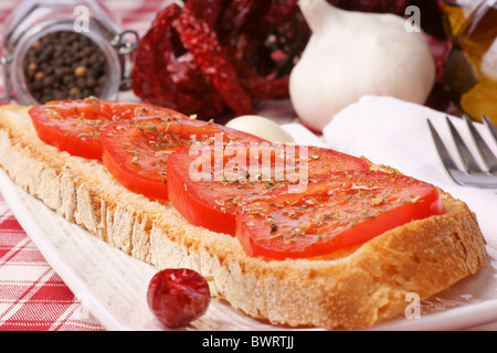 Pain grillé garni de tomate, huile d'olive et l'origan servi sur une plaque blanche Banque D'Images