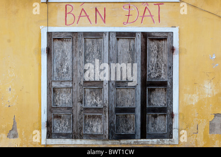 Double portes en bois situé dans un cadre blanc contre un mur jaune avec les mots vietnamiens 'Ban dat' peint en rouge Banque D'Images