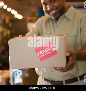 African American deliveryman holding out fort avec 'fragile' sticker Banque D'Images