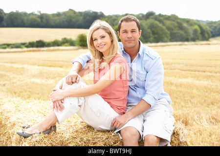 Couple assis sur des bottes de paille dans les champs récoltés Banque D'Images