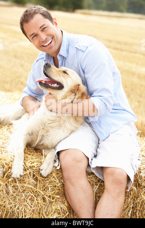 Homme assis avec chien sur des bottes de paille dans les champs récoltés Banque D'Images
