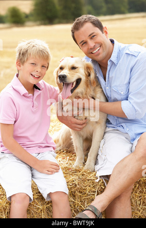 Père et fils assis avec chien sur des bottes de paille dans les champs récoltés Banque D'Images