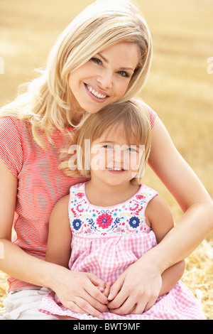 La mère et la fille assis sur des bottes de paille dans les champs récoltés Banque D'Images