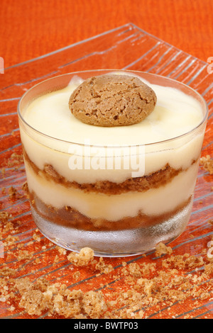Close-up de la crème à la vanille et de l'amaretto dessert servi dans une tasse en verre sur un fond orange. Focus sélectif. Banque D'Images