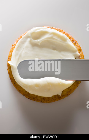 Propagation d'une spatule sur un fromage crémeux cracker sur un fond blanc. Banque D'Images