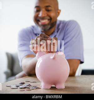 Smiling African American man putting coins in piggy bank Banque D'Images