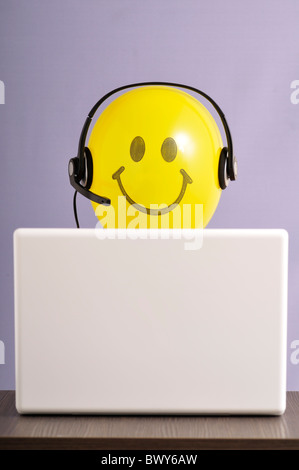 Smiley Face Balloon avec casque at laptop computer Banque D'Images