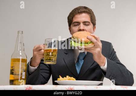 L'homme de manger un hamburger avec des frites, boire de la bière Banque D'Images