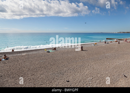 Un avion décolle de l'aéroport à l'horizon alors que le soleil vous détendre sur la plage à Nice, France. Banque D'Images