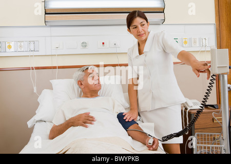 Infirmière en tenant la pression artérielle du patient in hospital room Banque D'Images