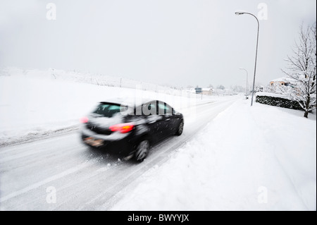 Une voiture roule sur une route couverte de neige dans une ville Suisse. Motion Blur sur la voiture. Banque D'Images