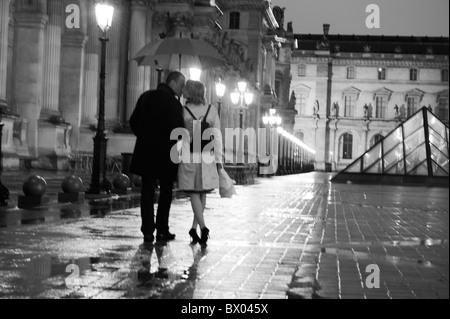 Caucasian couple kissing in rain la nuit au Louvre Banque D'Images