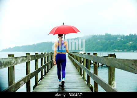 Caucasian woman in sportswear avec parapluie rouge sur la jetée Banque D'Images