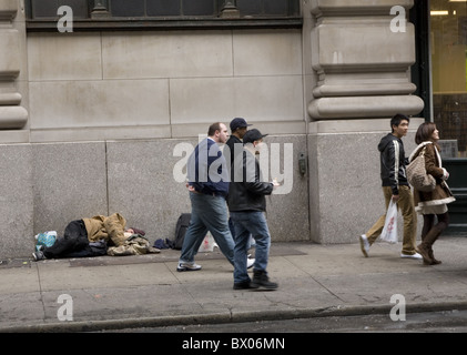 Les piétons à pied par un sans-abri dormant sur le trottoir à New York City. Banque D'Images