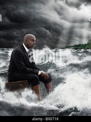 African American businessman sitting on suitcase in stormy sea Banque D'Images