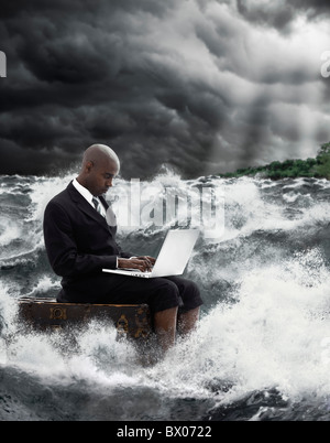 African American businessman using laptop in stormy sea Banque D'Images