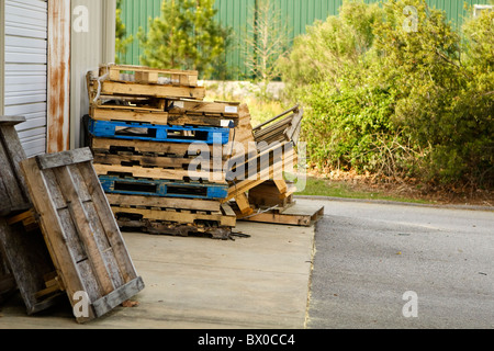 Des piles de palettes en bois Palettes aka derrière un bâtiment métallique industriel léger dans l'après-midi. Cette zone est utilisée pour les livraisons. Banque D'Images