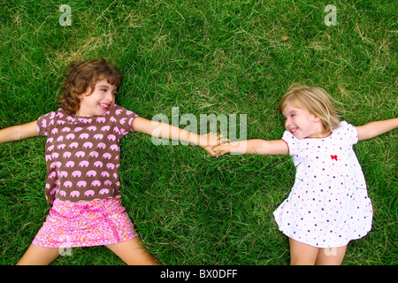 Deux sœur girls lying on meadow Green grass comme amis jouant Banque D'Images