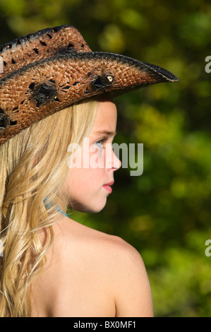 Très jolie cowgirl avec de beaux longs cheveux blonds portant un chapeau de cowboy, lâche et coule dans le parc naturel de la lumière du soleil de fin d'après-midi. Banque D'Images