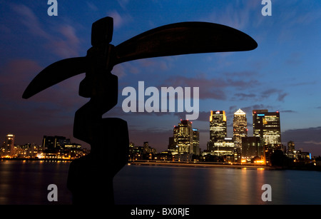 Les Docklands de Londres la Tamise et Canary Wharf au coucher du soleil avec la sculpture en silhouette au premier plan. Banque D'Images